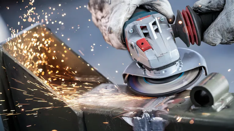 Uma pessoa que usa equipamento de segurança tritura metal, produzindo faíscas brilhantes.