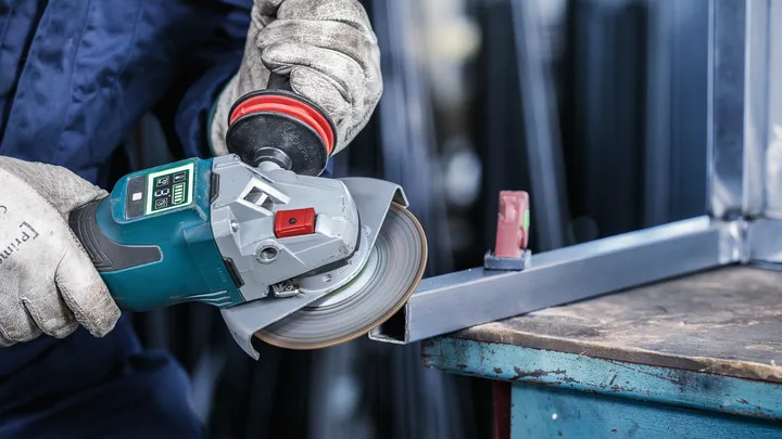 Uma pessoa que utiliza equipamento de segurança esmerilha uma estrutura metálica com uma esmerilhadora angular.