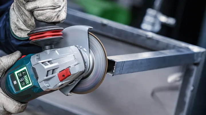 Uma pessoa que utiliza equipamento de segurança utiliza uma rebarbadora angular para cortar uma viga de metal.