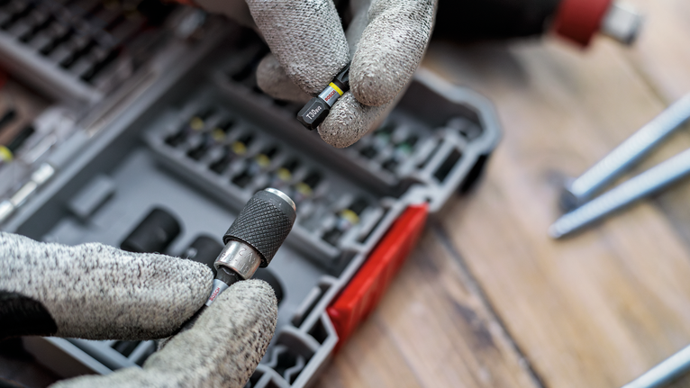 Uma pessoa que utilize equipamento de segurança seleciona uma ponta de chave de fendas de um estojo organizado.