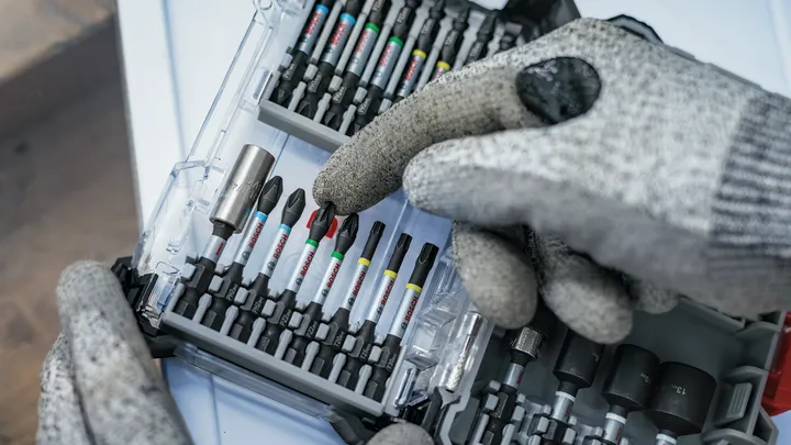 Uma pessoa que utiliza equipamento de segurança seleciona uma ponta de chave de fendas de um kit de ferramentas organizado.