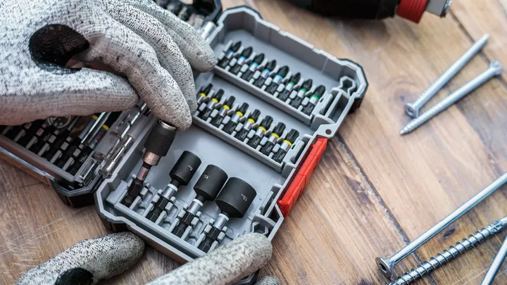 Uma pessoa que utilize equipamento de segurança seleciona uma ponta de chave de fendas de um estojo organizado.