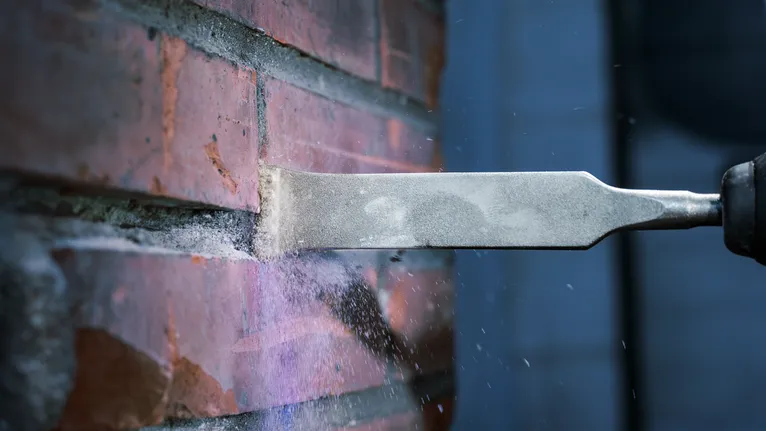 O cinzel remove a argamassa da parede de tijolos, espalhando o pó.