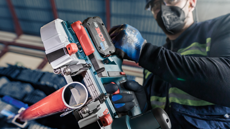 Uma pessoa que usa equipamento de segurança utiliza uma ferramenta elétrica para cortar um cano de metal.