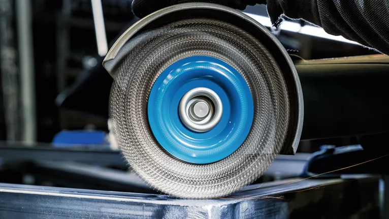 Uma pessoa que usa equipamento de segurança tritura metal com uma roda abrasiva giratória.