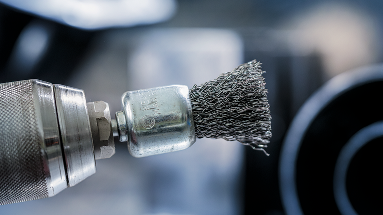 Ferramenta rotativa com escova de arame metálico utilizada para limpeza de superfícies.