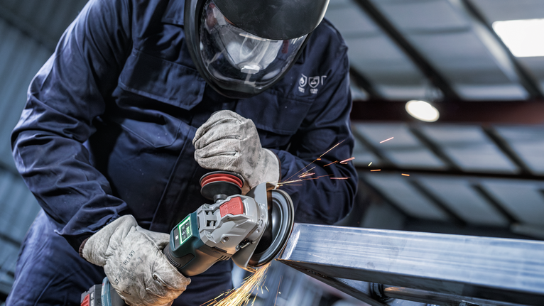 Uma pessoa que usa equipamento de segurança tritura metal, criando faíscas.