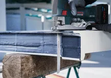 Uma pessoa que utiliza equipamento de segurança utiliza uma serra alternativa para cortar uma viga metálica.