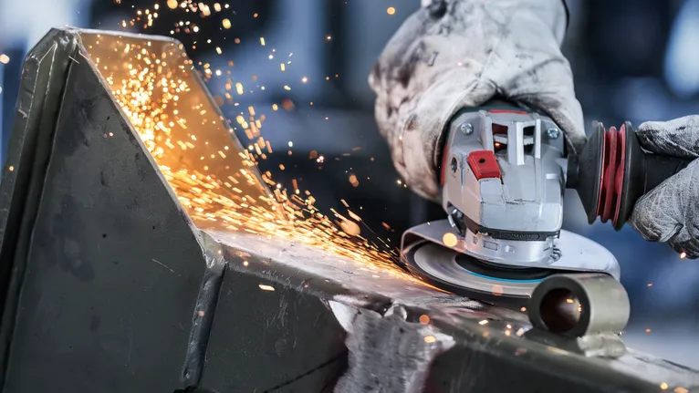 Pessoa que utiliza equipamento de segurança esmerilamento metal com rebarbadora angular, produzindo faíscas.