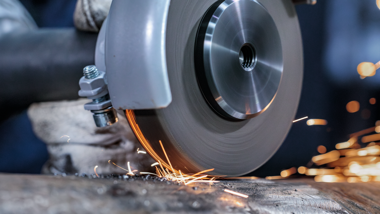 Uma pessoa que utiliza equipamento de segurança tritura metal com uma ferramenta elétrica, produzindo faíscas.