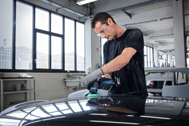 Uma pessoa que usa equipamento de segurança lustra o capô de um carro numa oficina mecânica.