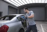 Uma pessoa que utiliza equipamento de segurança utiliza uma serra alternativa para cortar a moldura do vidro traseiro de um automóvel.