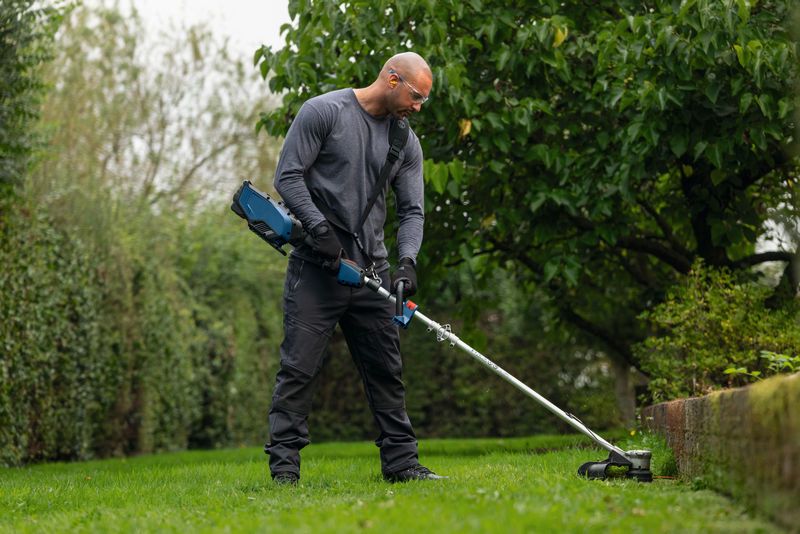 Uma pessoa que utilize equipamento de segurança apara a relva ao longo da borda do jardim com uma ferramenta sem fios.