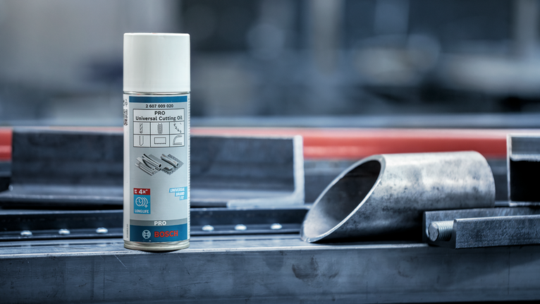 Lata de spray de óleo de corte colocada sobre uma bancada de metal ao lado de tubos de aço.