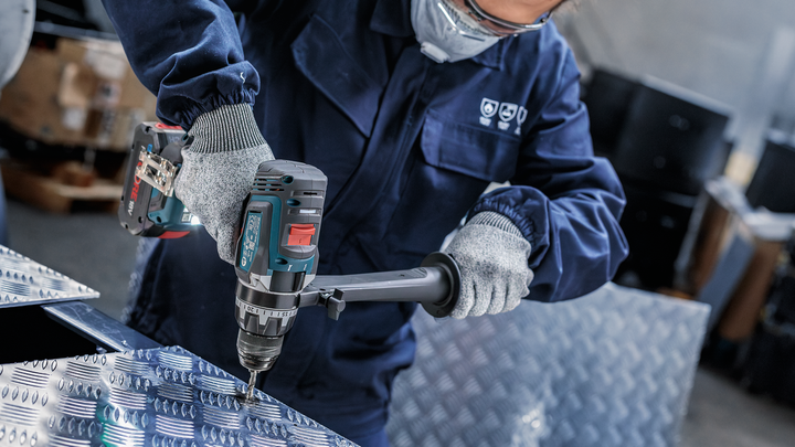 Uma pessoa que utilize equipamento de segurança perfura uma chapa metálica normalizada.