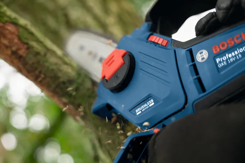 Uma pessoa que utilize equipamento de segurança utiliza uma motosserra azul para cortar um ramo de árvore.