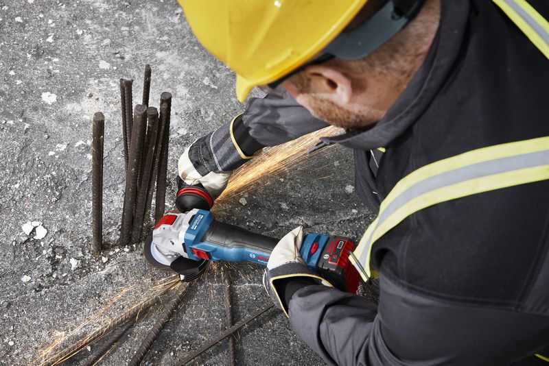 Uma pessoa que utiliza equipamento de segurança tritura varões numa superfície de betão com uma rebarbadora angular.