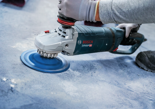 Uma pessoa que utilize equipamento de segurança lustra um piso de betão com uma ferramenta elétrica.