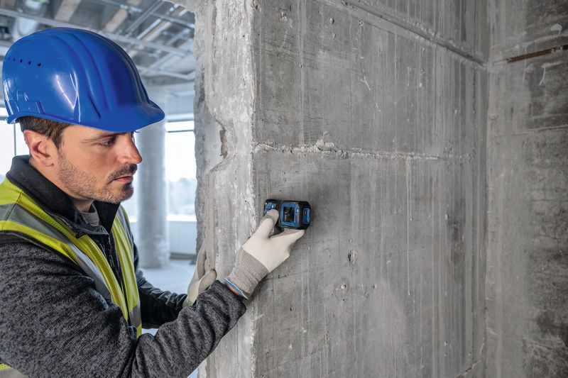 Pessoa que usa equipamento de segurança utiliza um medidor laser contra uma parede de betão.