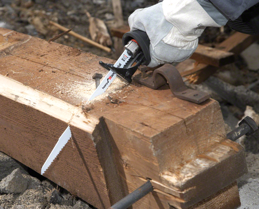 Um trabalhador que utilize equipamento de segurança utiliza uma serra alternativa para cortar uma viga de madeira.