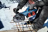 Uma pessoa que utiliza equipamento de segurança corta varões num estaleiro de obras com uma rebarbadora angular sem fio.