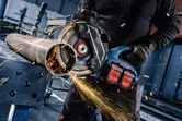 Uma pessoa que usa equipamento de segurança corta um cano de metal com uma rebarbadora sem fios.
