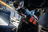 Uma pessoa que utiliza equipamento de segurança tritura metal com uma rebarbadora angular sem fios, produzindo faíscas.