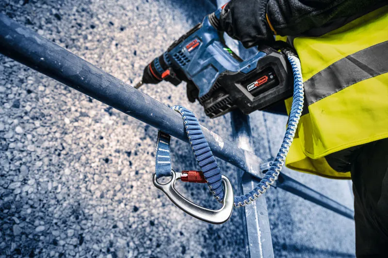 Uma pessoa que utiliza equipamento de segurança perfura metal utilizando um martelo rotativo sem fios.