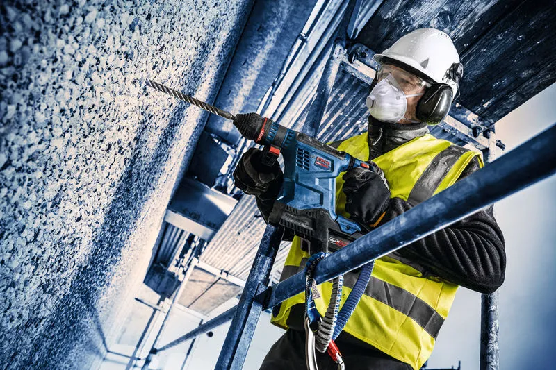 Uma pessoa que utiliza equipamento de segurança perfura o betão com um martelo rotativo sem fios.