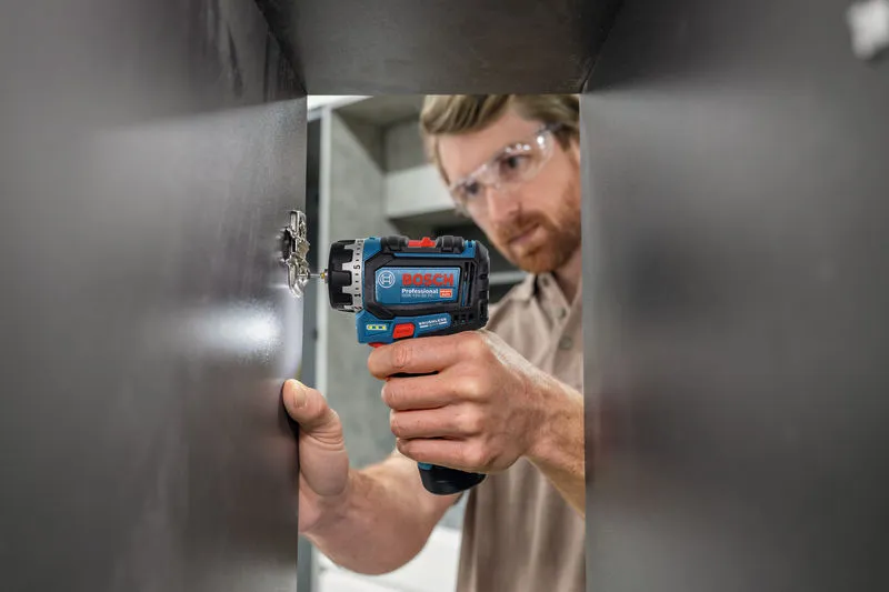 Uma pessoa que utiliza equipamento de segurança utiliza uma chave de fendas para instalar uma dobradiça de armário.