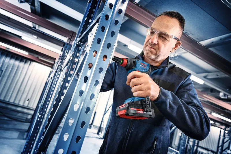 Uma pessoa que usa equipamento de segurança utiliza uma chave de impacto numa estrutura metálica.