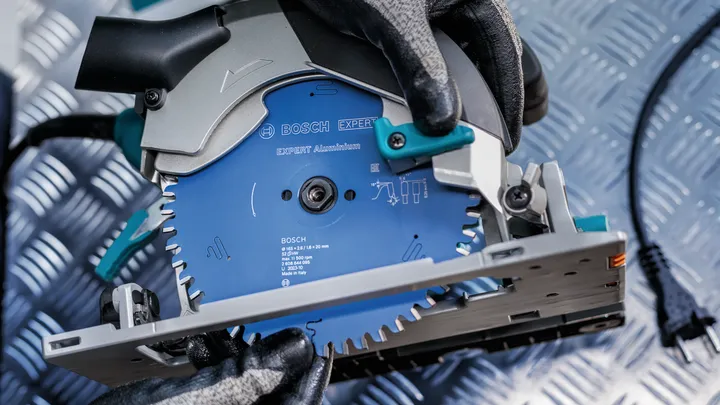 Uma pessoa que utilize equipamento de segurança ajusta uma serra circular numa superfície com um padrão metálico.