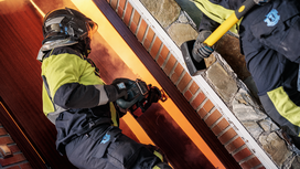 Uma pessoa que utiliza equipamento de segurança utiliza uma ferramenta elétrica para cortar uma porta durante uma emergência.