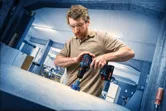 Uma pessoa que utilize equipamento de segurança perfura uma superfície de trabalho com um berbequim sem fio.