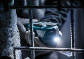 Uma pessoa que usa equipamento de segurança utiliza um corta-relva múltiplo sem fios com uma luz LED perto de uma barra de ferro.