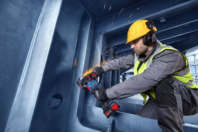 Uma pessoa que utiliza equipamento de segurança utiliza uma rebarbadora angular para cortar metal dentro de uma estrutura grande.