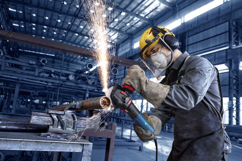 Uma pessoa que utiliza equipamento de segurança tritura um tubo de metal, produzindo faíscas numa fábrica.