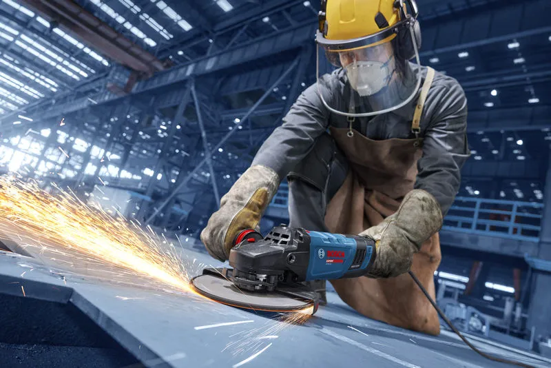 Uma pessoa que usa equipamento de segurança tritura metal, produzindo faíscas brilhantes.