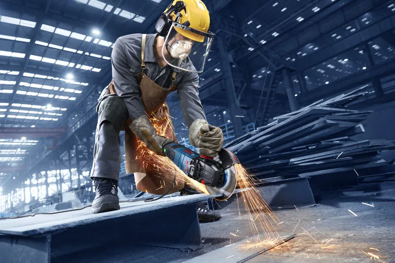 Uma pessoa que utiliza equipamento de segurança utiliza uma rebarbadora angular para cortar metal, produzindo faíscas.