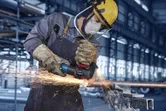Uma pessoa que usa equipamento de segurança tritura um cano de metal, criando faíscas brilhantes.