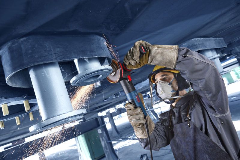 Uma pessoa que usa equipamento de segurança tritura metal acima da cabeça com uma rebarbadora, criando faíscas.