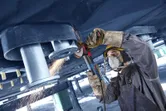 Uma pessoa que usa equipamento de segurança tritura metal acima da cabeça com uma rebarbadora, criando faíscas.