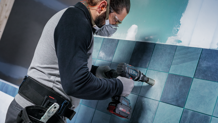 Pessoa que usa equipamento de segurança perfura um buraco em azulejos de cerâmica.