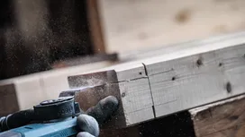 Pessoa que utiliza equipamento de segurança lixa uma tábua de madeira com uma ferramenta elétrica.