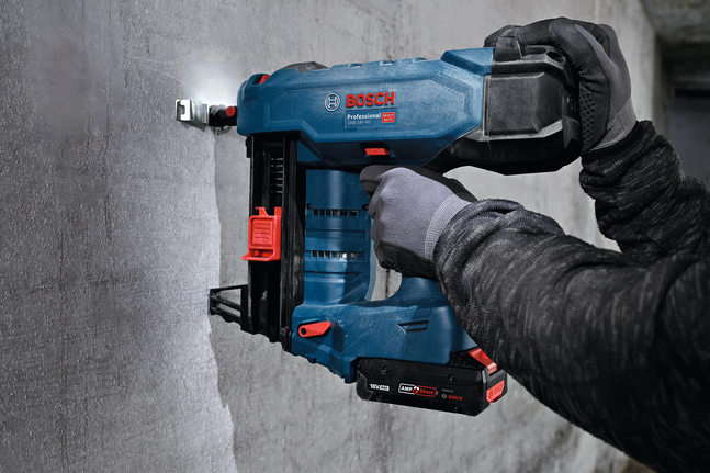 Uma pessoa que utiliza equipamento de segurança fixa um suporte metálico para abraçadeiras de nylon a uma parede de betão.