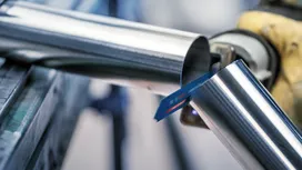 Pessoa que utiliza equipamento de segurança a cortar um tubo de metal com uma serra recíproca.