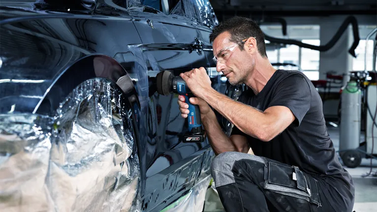 Pessoa que usa equipamento de segurança lustra a porta de um carro com uma ferramenta sem fios.