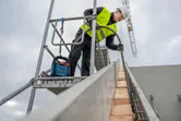 Pessoa que utiliza equipamento de segurança a trabalhar em andaimes num canteiro de obras.
