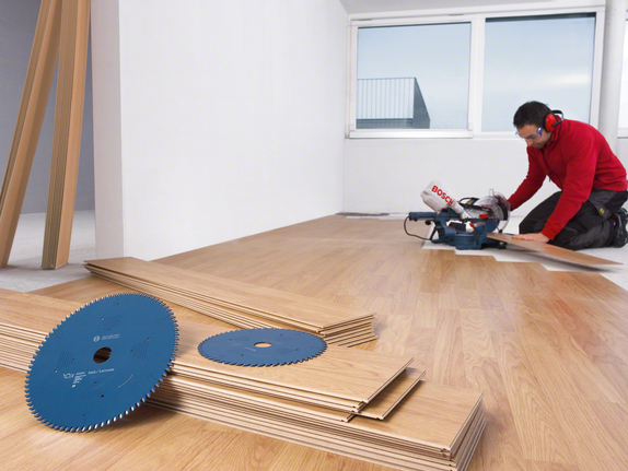 Trabalhador que utiliza equipamento de segurança corta pavimento laminado com uma serra de esquadria.