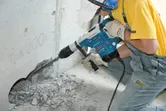 Una persona que usa equipo de seguridad perfora hormigón con un martillo perforador.